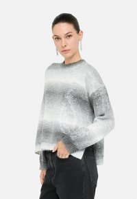 Pulover rayat gri și alb cu guler rotund, mâneci lungi și croi lejer. Tricotat texturat cu efecte subtile de strălucire.