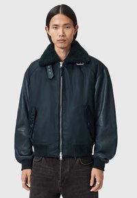 Tummansininen bomber-takki, jossa suuri, teksturoitu musta tekoturkiskaulus; takissa on vetoketjusuljenta, sivutaskut sekä resorit hihansuissa ja helmassa.