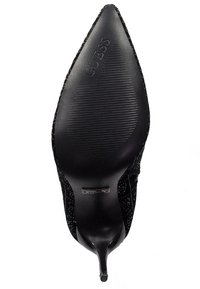 Décolleté nera a punta con tomaia in tessuto testurizzato, sottile tacco a stiletto e suola rigata con il nome del brand "GUESS."