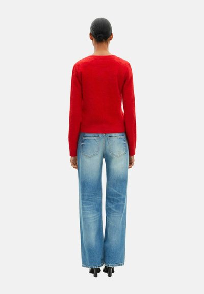 Rød, tekstureret sweater med lange ærmer parret med blå, brede jeans. Sweateren har en rund halsudskæring. Simpelt, afslappet outfit.