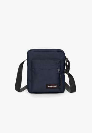 Mørkeblå skuldertaske lavet af slidstærkt stof, med en frontlomme med lynlås, justerbar rem og Eastpak-logo på forsiden.