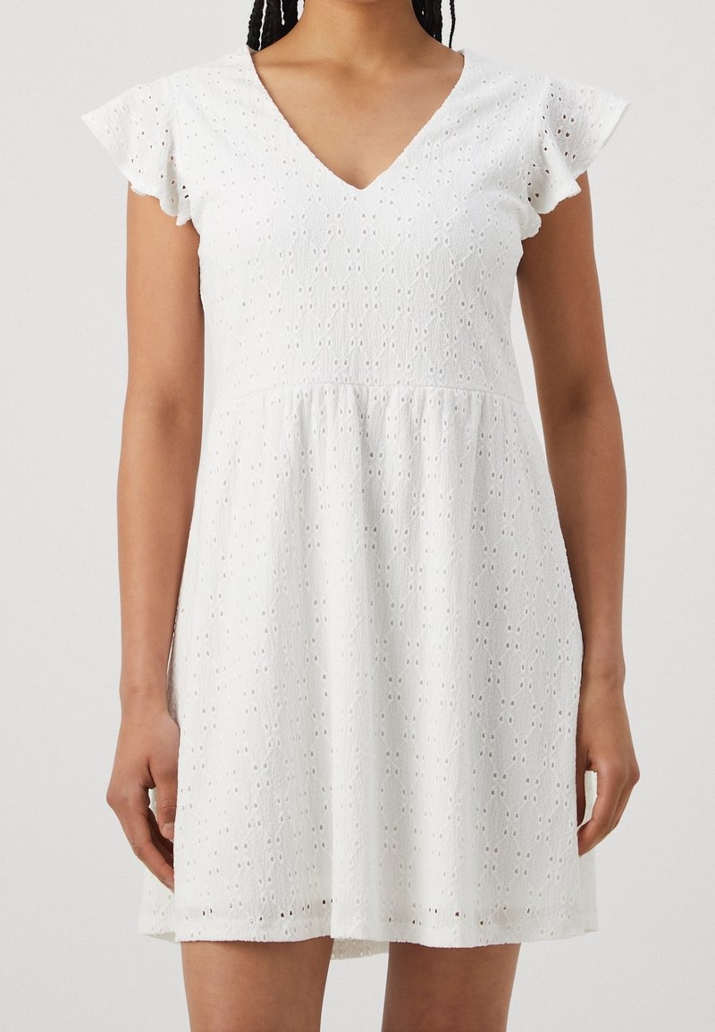 Femme portant une robe blanche à manches courtes, col en V, avec un motif en dentelle ajourée et une jupe évasée.