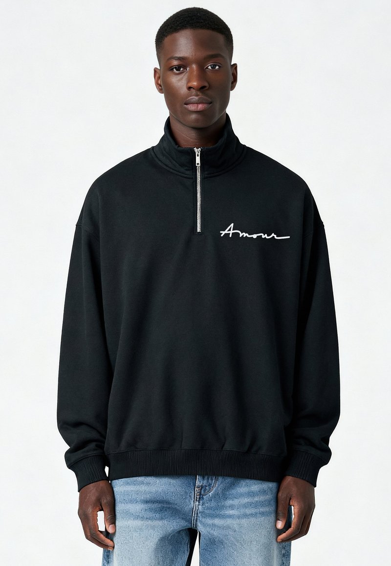 Sweatshirt noir à demi-fermeture éclair avec "Amour" en cursive blanche sur la poitrine. Comprend des poignets et un bas côtelés, fabriqué en coton doux.