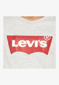 Pilkas medvilnės marškinėliai su apvaliu kaklu, kuriuos puošia išsiskiriantis raudonas "Levi's" logotipas su baltu tekstu priekyje, atskleidžiantis prekės ženklo ikoninį dizainą.
