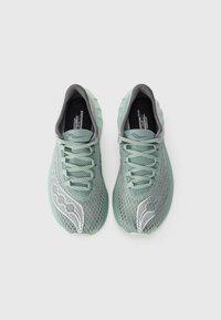 Baskets de sport vert clair avec une tige en maille, accents gris, semelle texturée et détails réfléchissants argentés sur le côté.