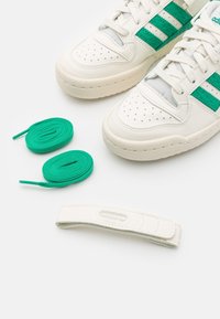 Vita sneakers med gröna accenter och tre ränder, med perforerat tåparti, slätt läder, två gröna skosnören och ett märkesband.