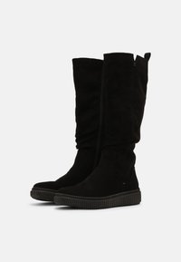 Bottes hautes jusqu'au genou en daim noir avec une semelle en caoutchouc texturée et une fermeture éclair latérale. Présentent un design décontracté et des accents cousus pour plus de détails.