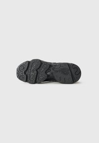 Black rubber sneaker outsole with a textured tread pattern, featuring circular and wavy designs for traction and stability.