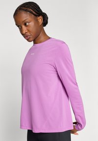 Αθλητική μπλούζα μακρυμάνικη σε ανοιχτό μοβ χρώμα, υφασμάτινη με υφή, στρογγυλή λαιμόκοψη, λεπτομέρειες σε αντίθετη ραφή, λογότυπο στο στήθος, εφαρμοστή σιλουέτα.