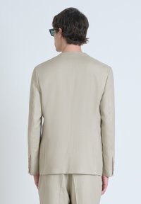 Giacca da suit beige su misura con una texture liscia e una fessura singola sul retro. Presenta maniche lunghe e dettagli di cucitura sottili.
