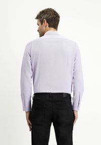 Camicetta lunga a maniche viola chiaro con colletto strutturato, pieghe sul retro e bottoni neri, abbinata a jeans neri. Tessuto leggermente testurizzato.