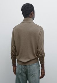 Brown knitted sweater with a ribbed collar and cuffs, paired with light denim jeans, featuring a relaxed fit and subtle texture.