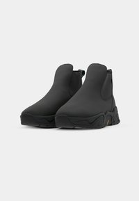 Black ankle boots with textured soles, featuring a smooth upper and elastic side panels for easy wear. Set against a white background.