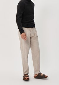 Col roulé noir, pantalon à rayures claires et sandales marron. Les caractéristiques clés incluent un design ajusté, une texture tissée et des chaussures confortables.