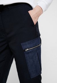 Mörkblå cargobyxor med en texturerad denimficka, med dragkedjestängning. Materialet verkar hållbart med en slät yta.