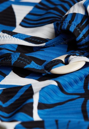 Tkanina za kupaće kostime s apstraktnim uzorcima u plavoj i crnoj boji, s bijelim akcentima. Uključuje veliki, glatki gumb i vidljive šavove.