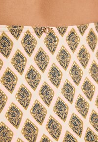 Vzorovaná látka so zlatými a tmavomodrými diamantmi na svetloružovom pozadí, s dekoratívnou sponou v páse.