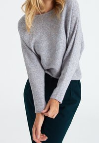 Pull gris clair à côtes avec coupe ample et large encolure, associé à un pantalon vert foncé texturé. Tissu lisse avec des variations de couleur subtiles.