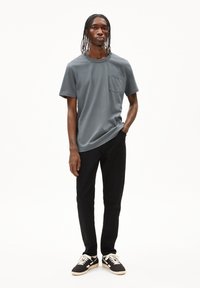 Grijze T-shirt met korte mouwen en een borstzak, gecombineerd met zwarte broek en zwarte sneakers met witte accenten en een gestructureerde zool.