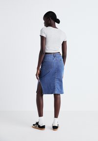 Džinsu svārki ar sānu izgriezumu, zila krāsa, virs ceļgala garums. Kombinēti ar pelēku īso t-kreklu un melniem sporta apaviem ar baltām akcentiem.