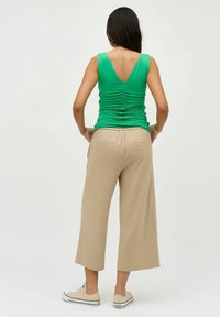 Zelený bezrukávový top s řasením vzadu, zkombinovaný s béžovými kalhotami s volným střihem. Oblečení doplňují béžové tenisky.