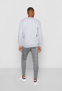 Jasnoszara bluza z ribbowanymi mankietami i paskiem, w połączeniu z dopasowanymi czarno-białymi spodniami w kratę oraz białymi sneakersami.