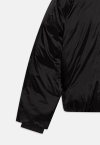 Giacca nera imbottita realizzata in un tessuto lucido e liscio, con silhouette oversize, polsini a coste e orlo corto.