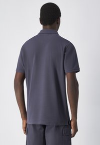 Granatowa koszulka polo z krótkimi rękawami, klasycznym kołnierzykiem i gładką teksturą. Widok z tyłu podkreśla minimalistyczny design bez zdobień.