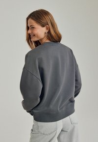 Ciemnoszara, oversize bluza z okrągłym dekoltem i opuszczonymi ramionami, z prążkowanymi mankietami i dołem. Miękka, teksturowana tkanina.