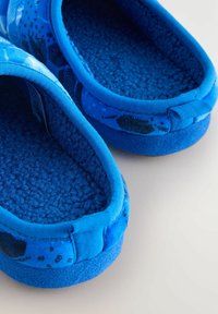 Blå tygtofflor med mjuk textur, med en fluffig inredning, rund form och designmönster i mörkare nyanser av blått.