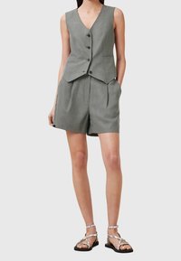 Gilet en lin gris avec un col en V et cinq boutons, associé à un short taille haute assorti et des sandales à lanières argentées.