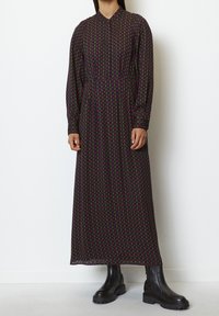 Robe longue noire avec un motif géométrique de formes rouges et jaunes, dotée d'un col et de manches longues. Assortie à des bottes noires à semelles épaisses.