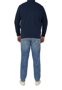 Felpa blu navy con collo alto, abbinata a jeans in denim azzurro. I jeans presentano una texture sbiadita e tasche posteriori standard.