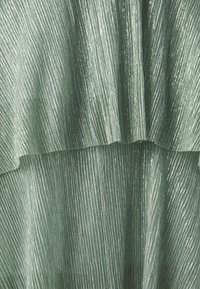 Gros plan d'un tissu vert plissé avec un éclat métallique et une texture en couches.