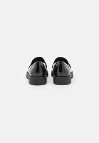 Paire de mocassins en cuir verni noir vue de dos sur un fond blanc uni.
