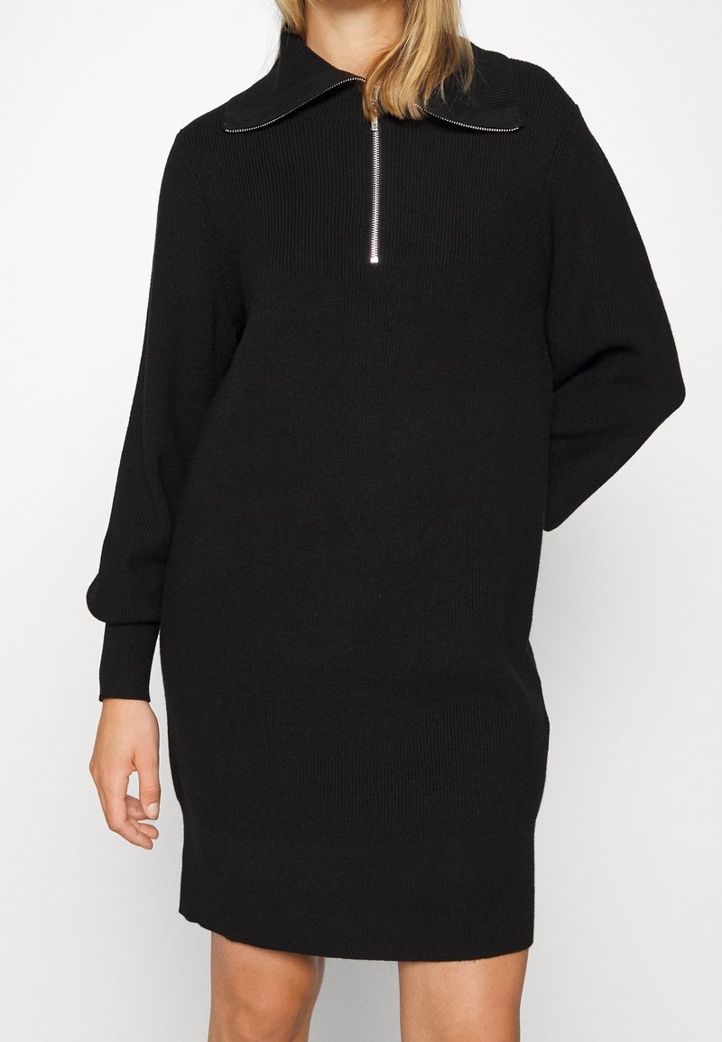 Svart stickad klänning med hög krage och dragkedja, långa ärmar med ribbade manschetter och en avslappnad passform.