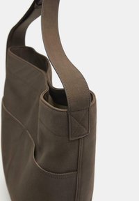 Smeđa kožna torba s čvrstom konstrukcijom, koja ima dvije vanjske bočne džepove i široku ravnu naramenicu.