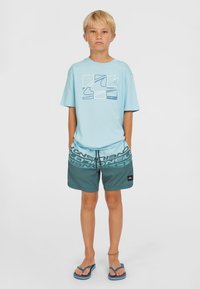 Ljusblå t-shirt med grafisk design, kombinerad med mörkgröna badshorts med en iögonfallande logotryck. Avslappnade flip-flops fulländar looken.