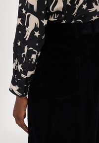Pantalon en velours côtelé noir avec poche arrière et chemise noire à manches longues avec des motifs beige de chat et d'étoiles.