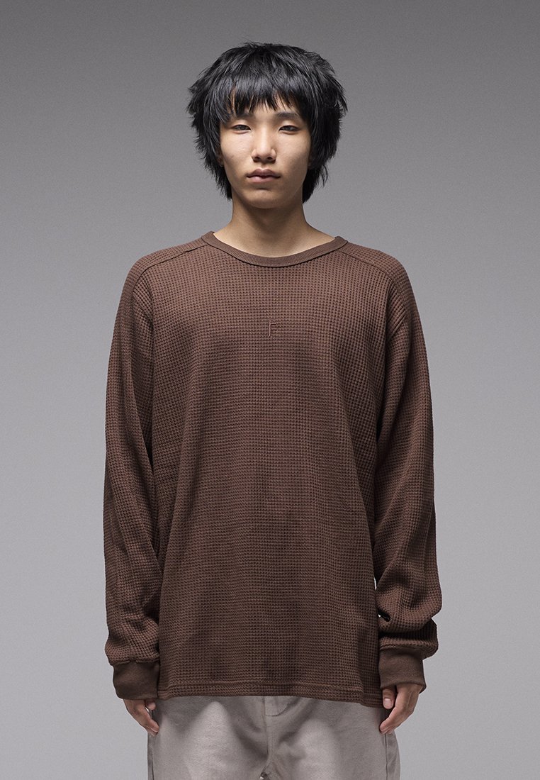 Chemise marron à manches longues avec un tissage gaufré texturé, col rond, et coutures d'épaule tombantes. Coutures minimales et aucun logo visible.