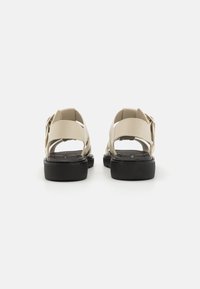 Beige sandalen met een modern ontwerp, een gestructureerd zwart plateau, brede banden en een gespaccent aan de achterkant.