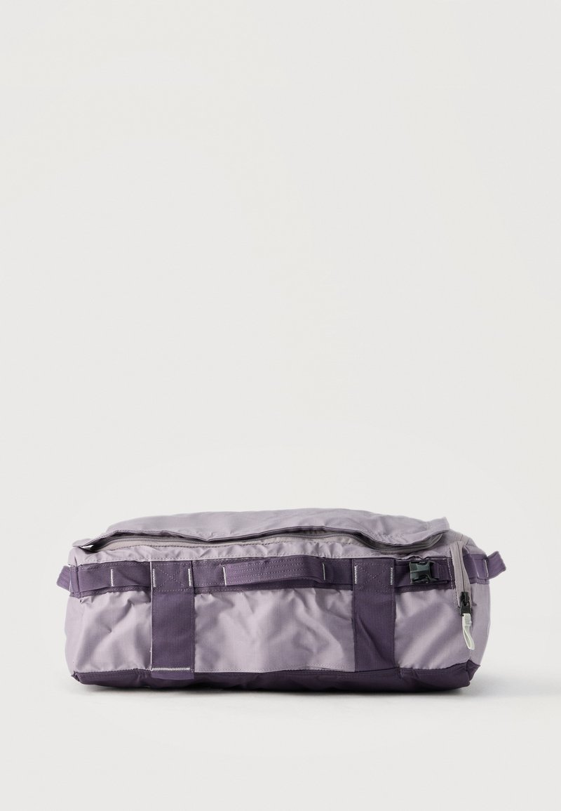 Διπλωμένη τσαντα duffel σε ανοιχτό μωβ και σκούρο μωβ χρώμα με πλαϊνή τσέπη με φερμουάρ και λουρί ασφαλείας με αγκράφα σε λευκό φόντο.