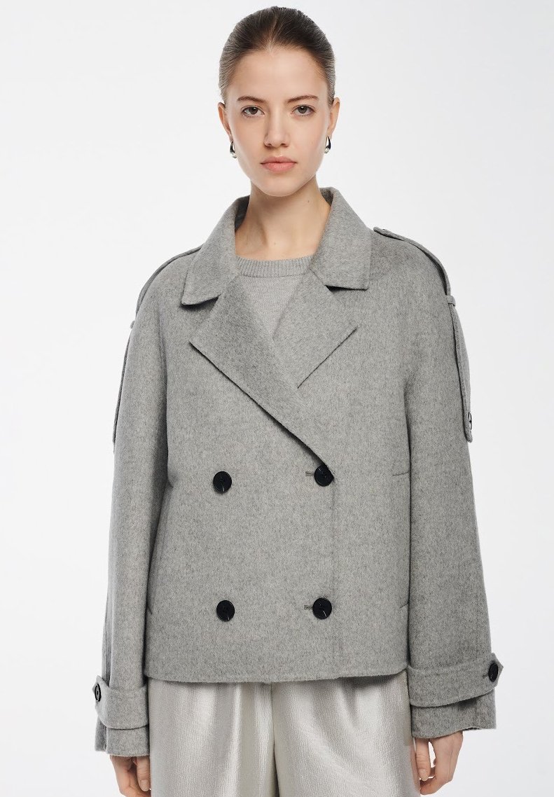 Cappotto grigio doppiopetto con una texture morbida, grandi bottoni neri, colletto ampio e spalline; presenta tasche a toppa e una vestibilità rilassata.