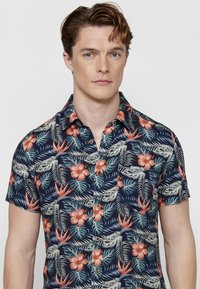 Korte mouwen overhemd met knopen op een marineblauwe achtergrond, versierd met tropische bloemenpatronen in tinten van koraal, groen en beige.