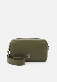 Crossbody taske i olivengrønt læder med lynlåslukning, guldfarvet hardware og en aftagelig rem med et signaturlogo på forsiden.