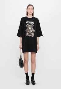 Svart oversized t-shirt klänning med en grafisk björntryck, korta ärmar och rund halsringning, kombinerad med svarta strumpor och loafers.