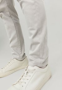 Chinos gris clair avec une coupe slim, fabriqués en tissu mélangé de coton. Présentent un ourlet soigné et sont associés à des baskets blanches.