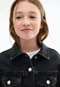 Črna denim jakna z vidnimi šivi, dvema sprednjima žepoma in belimi gumbi. Nosi se čez belo srajco. Lase ima valovite in dolge do ramen.