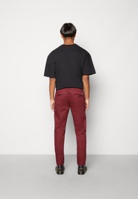 Camicia nera a maniche corte abbinata a pantaloni tailored color bordeaux. Tasconi posteriori visibili sui pantaloni e scarpe nere con suola texture.