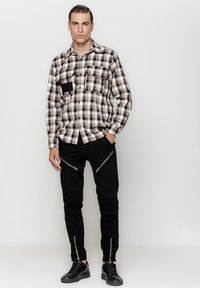 Koszula w kratę w beżowym, brązowym i czarnym kolorze; dwa kieszenie na piersi. Czarne spodnie z ukośnymi zamkami; czarne buty. Prosty, nowoczesny design.